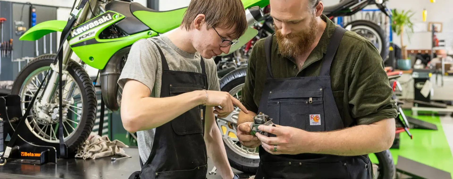 Docent en student staan voor motorfiets te kijken naar onderdeel