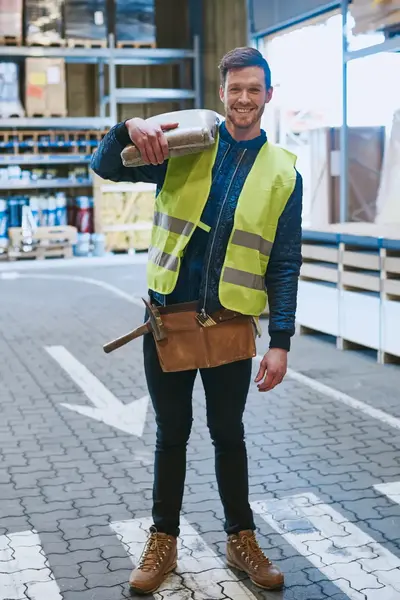 Man geel veiligheidshesje is een groothandel en heeft een zak cement op zijn schouders.