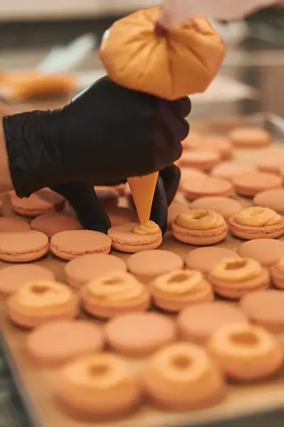 Student vult macarons met crème. Op de bakplaat liggen rijen verse macarons klaar om afgemaakt te worden.