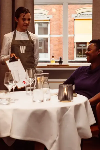 Warmoes-studente laat menu aan klant zien.