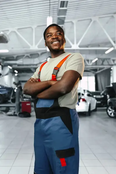 Automonteur in werkkleding poseert met armen over elkaar in garage.