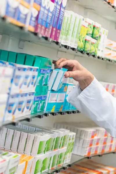 Apotheker in witte jas pakt een doosje medicijnen.