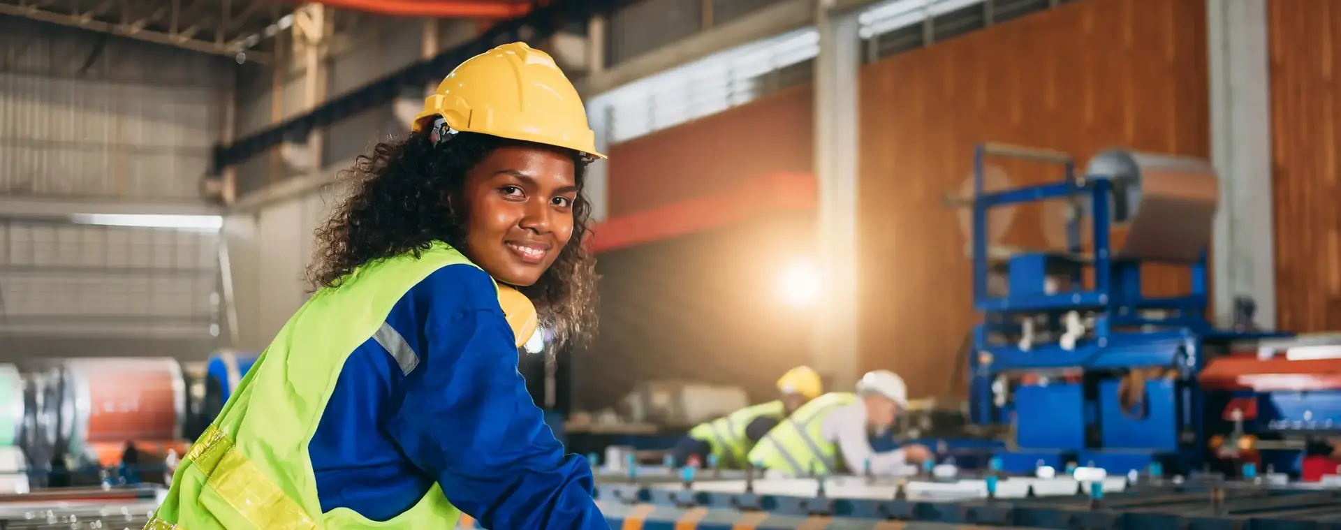 Vrouw met geel hesje en gele helm op staat voor een grote machine
