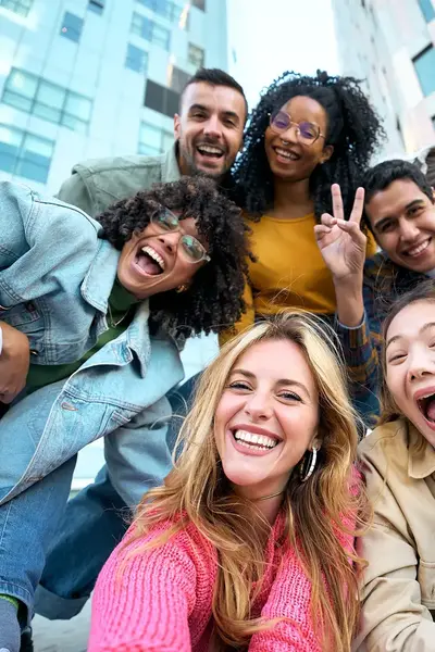Diverse groep lachende jongeren poseren met gebouwen op de achtergrond.