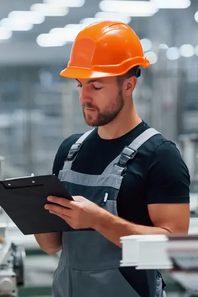 Man met helm en schrijfboard controleert machine