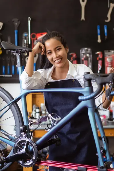 Fietsenmaker poseert naast frame racefiets in werkplaats