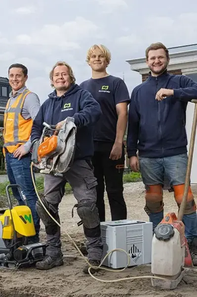 Vijf straatmakers in werkkleding staan op straat met apparatuur en lachen in de camera
