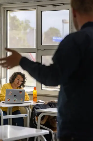 Docent geeft les aan studenten met laptops in klaslokaal.