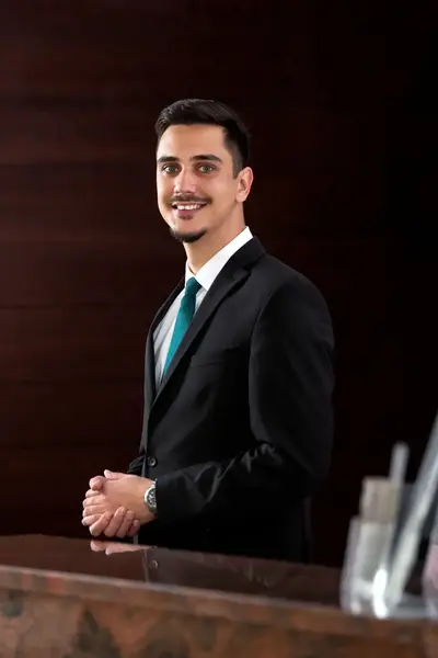 Man in pak achter hotelreceptie verwacht gasten.