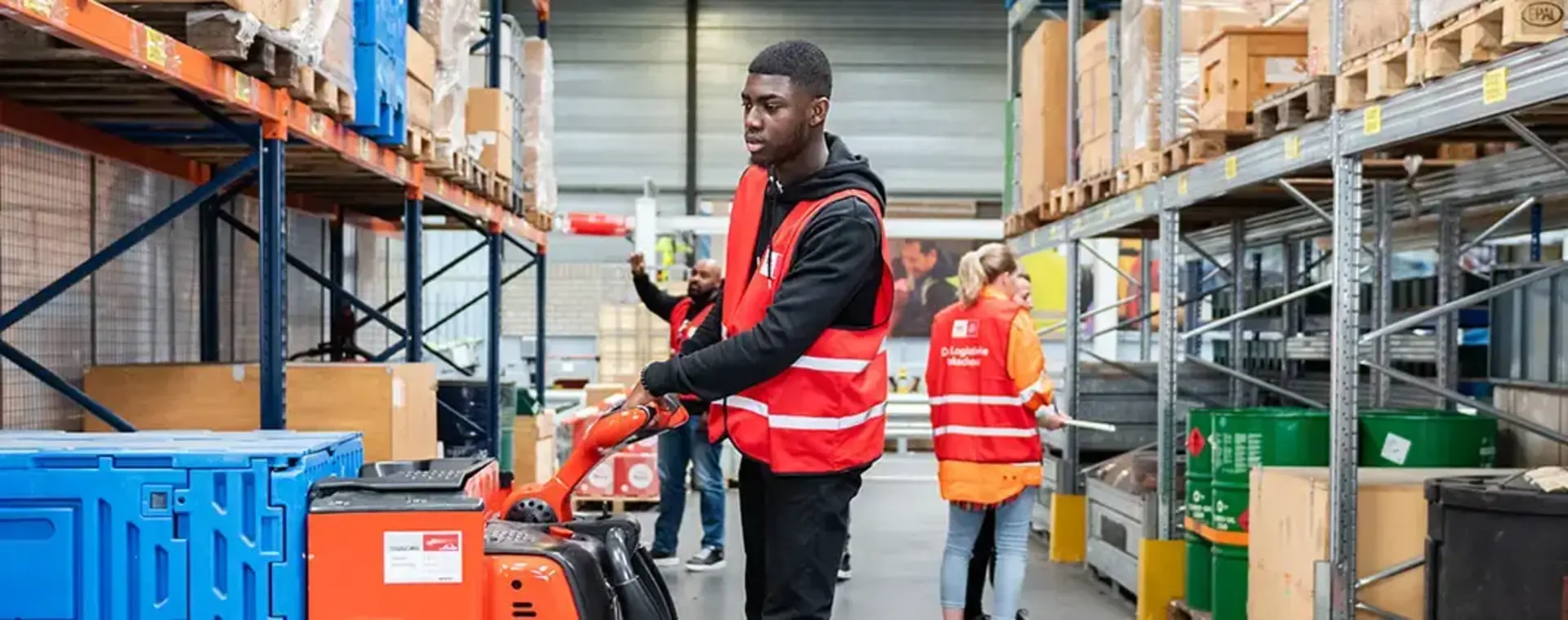 Student in rood hesje staat op een kleine vorkheftruck in een opslagloods.