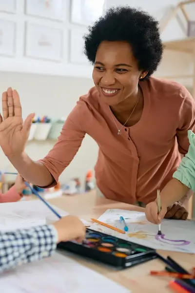 Juffrouw geeft kindje in klas een high-five tijdens schilderles.