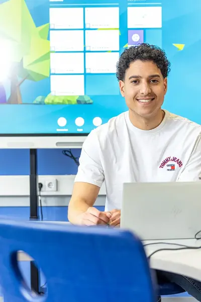 Jongen zit glimlachend achter zijn laptop.