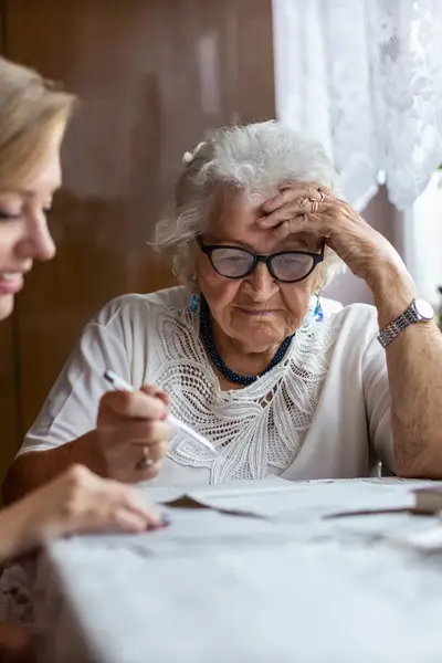 Oudere dame wordt door jonge dame geholpen met papierwerk.