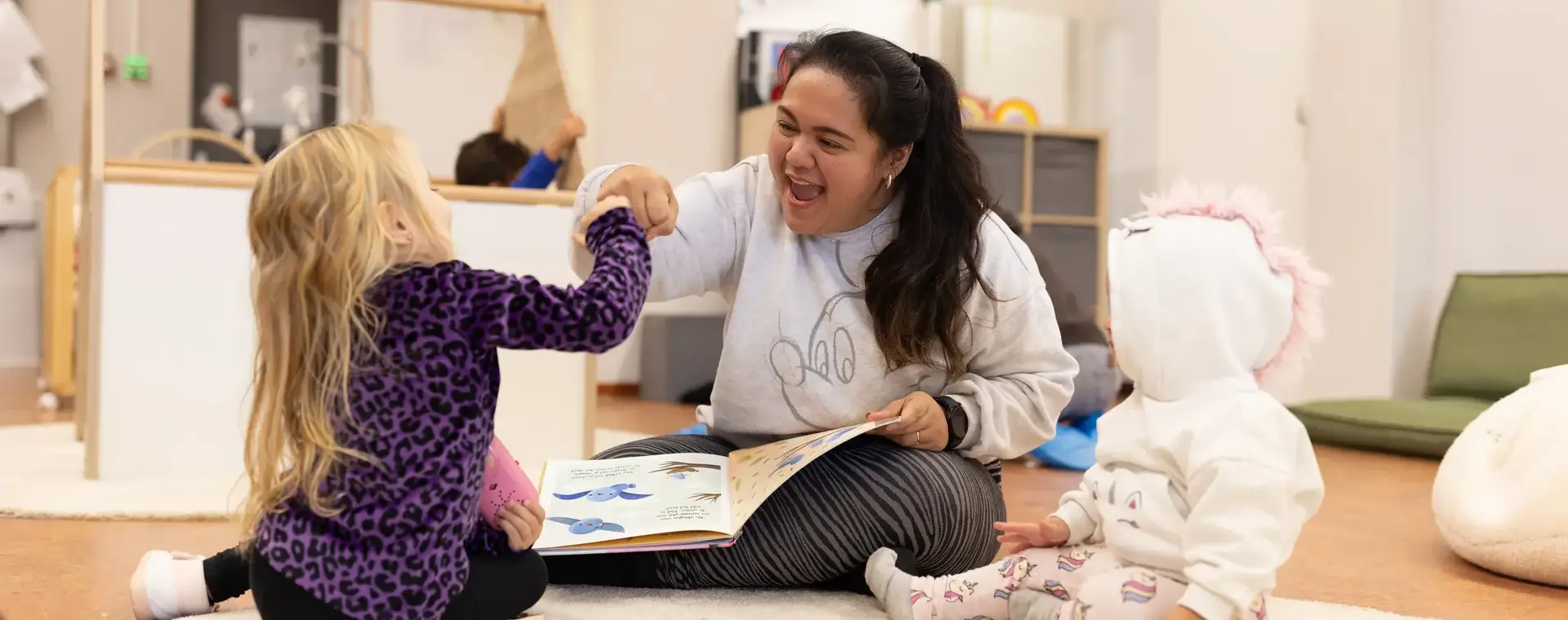 Juffrouw speelt met kleine kinderen op een kleed.