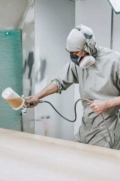 Coating specialist in grijze overall, gasmasker en verfspuit