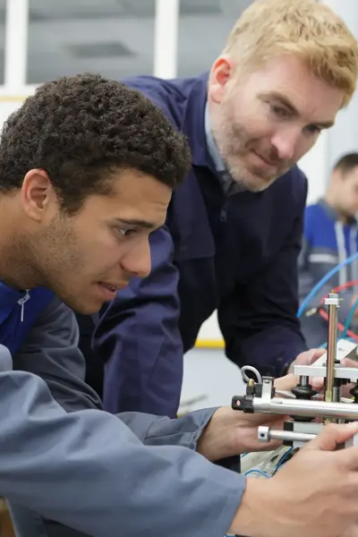 Docent helpt student in overall bij technische opdracht. 