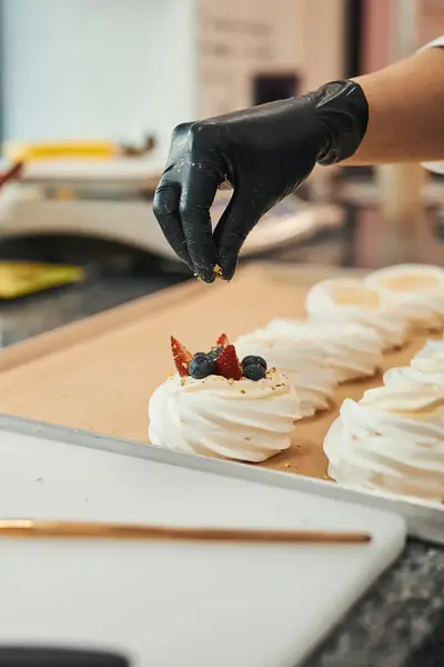 Student decoreert meringues met vers fruit. Op de werkbank liggen aardbeien, bosbessen en bakmaterialen klaar.