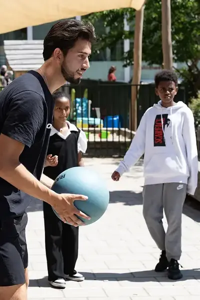 Student speel balspel met kinderen op schoolplein