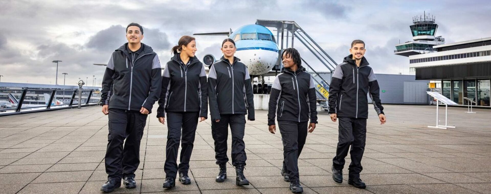 Studenten Luchthavenbeveiliger lopen over Schiphol met KLM-vliegtuig op de achtergrond