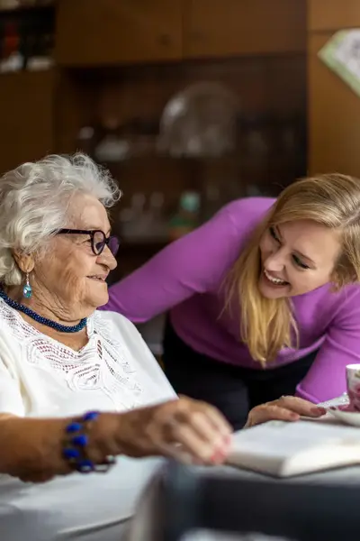 Zorgverlener heeft plezier met oudere dame die aan tafel zit