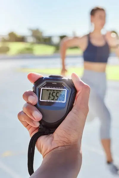 Drie sprinters rennen op atletiekbaan en hun tijd wordt gemeten door iemand met een stopwatch.