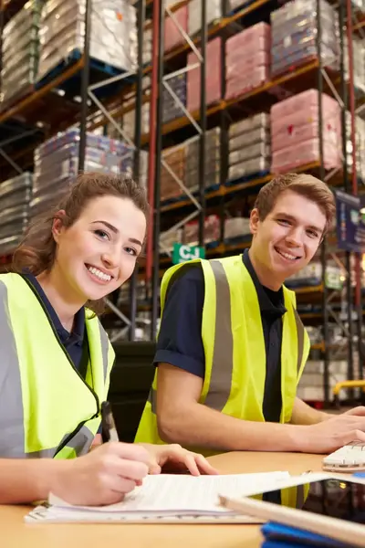 Twee in geel hesje geklede man en vrouw verwerken orders in een computer in een magazijn.