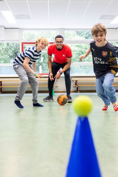 Kinderen rennen op bal af onder begeleiding sportstudent