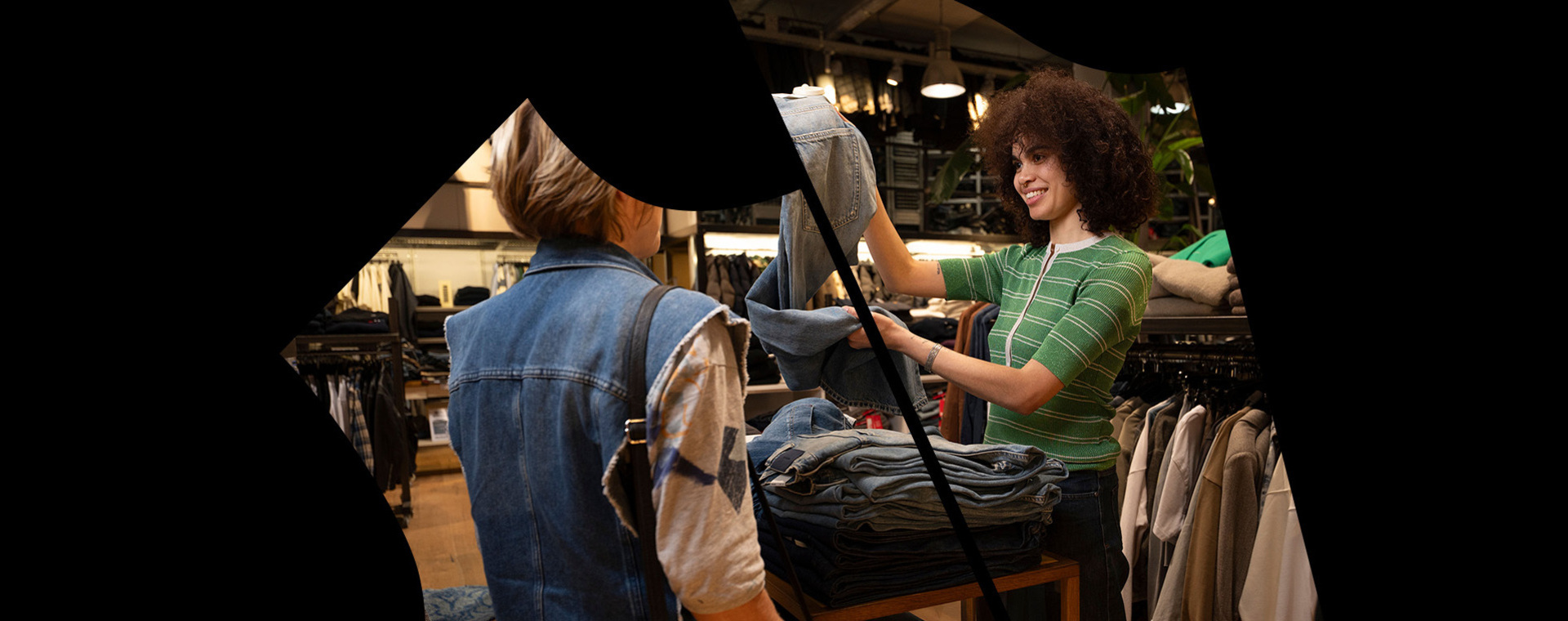 Verkoopster toont spijkerbroek aan dame in kledingwinkel