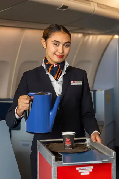 Vriendelijke stewardess schenkt drankjes in tijdens vlucht en staat met een trolley in het gangpad van het vliegtuig.
