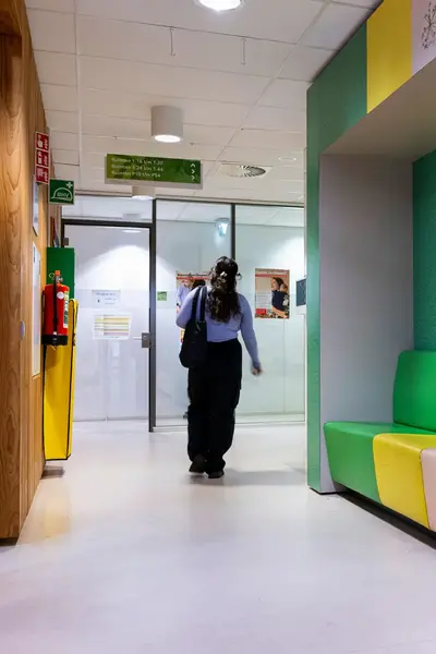 Student loopt door gang van schoolgebouw langs kleurrijke zitbanken.