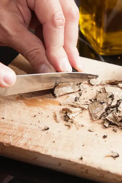 Kok snijdt truffel in fijne plakjes op snijplank