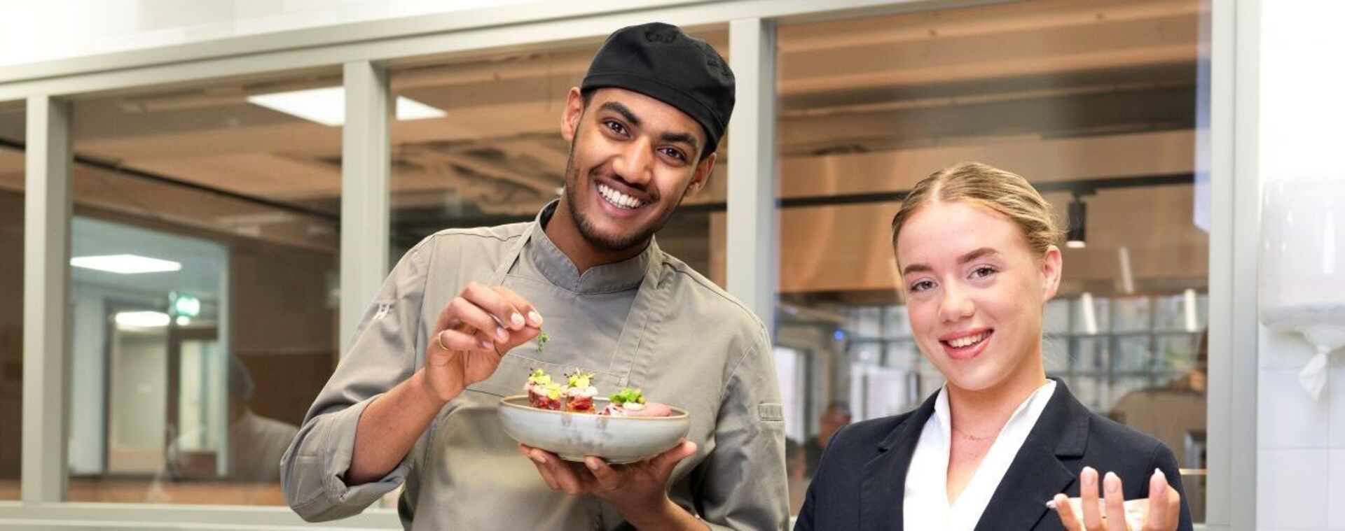 Horecastudenten in keuken poseren met gerechten en wijnglazen