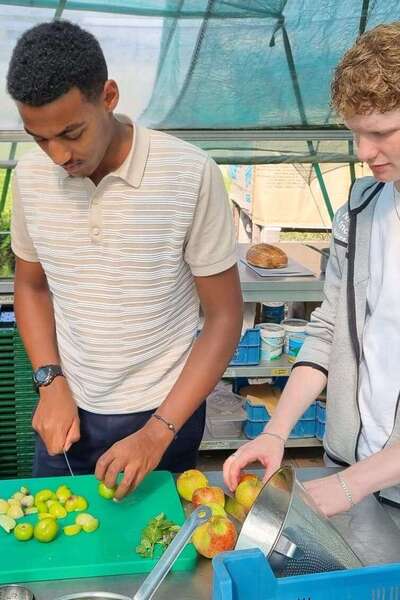 Kidus Houwen staat met twee studenten in een pluktuin groente te snijden.
