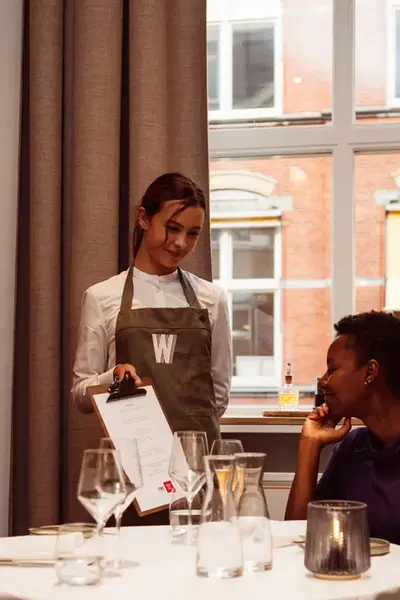 Studente in restaurant Warmoes laat het menu aan een klant zien.