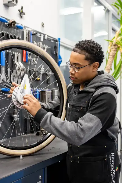 Student in werkkleding sleutelt aan voorwiel fiets in werkplaats
