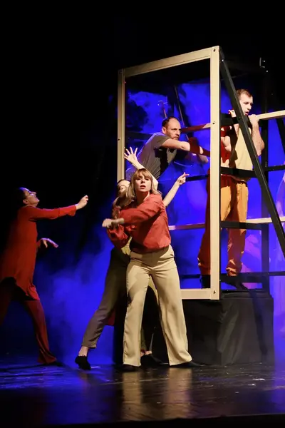 Groep spelers voert een theatervoorstelling op met een houten stellage op het toneel.