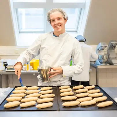 Student Bakker smeert broodjes in op bakplaat in praktijklokaal