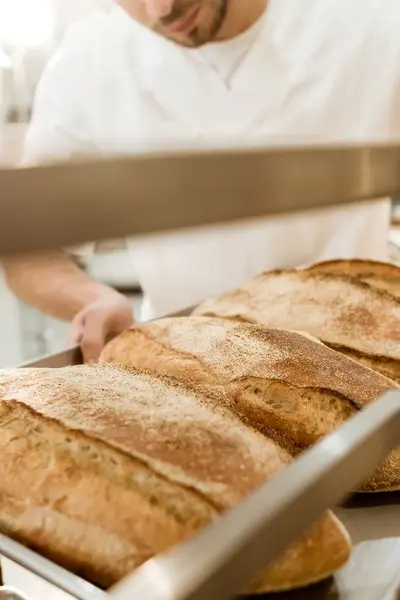 Bakker plaatst versgebakken broden op een rek.