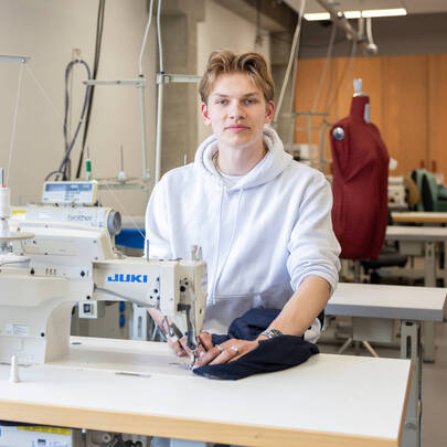 Jongen achter naaimachine kijkt recht de camera in.