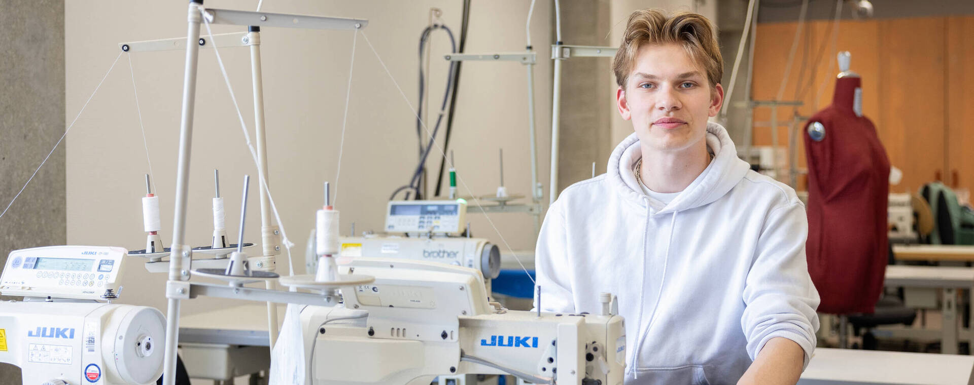 Jongen achter naaimachine kijkt recht de camera in.