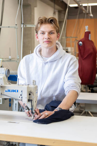 Jongen achter naaimachine kijkt recht de camera in.