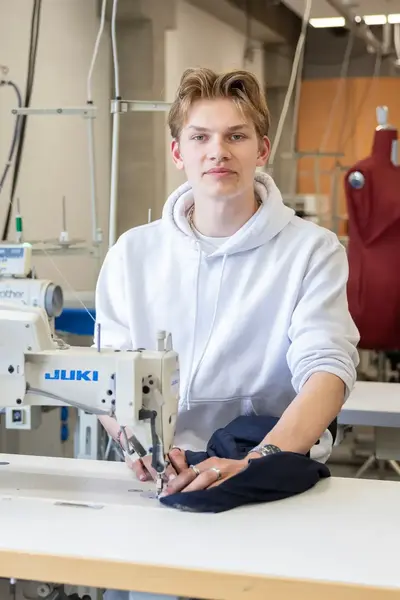 Jongen achter naaimachine kijkt recht de camera in.