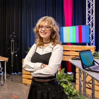 Studente in een studiosetting staat met haar armen over elkaar en kijkt recht de camera in.