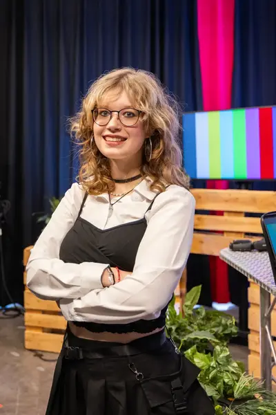 Studente in een studiosetting staat met haar armen over elkaar en kijkt recht de camera in.