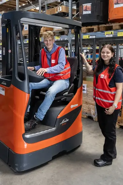 Student in rood hesje zittend in een vorkheftruck met student ernaast.