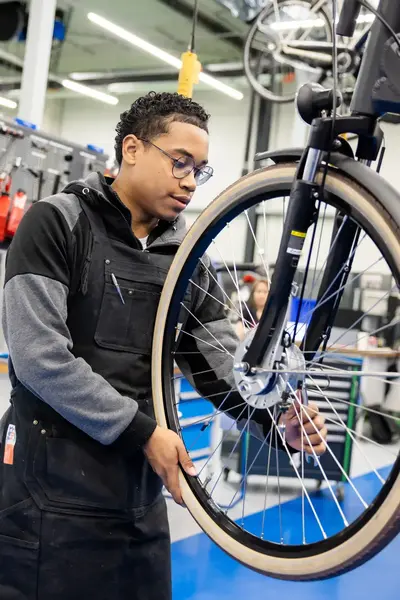 Student in werkkleding sleutelt aan voorband fiets in praktijklokaal