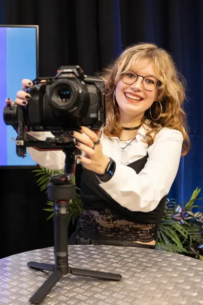 Mediastudent positioneert camera op desk met beeldscherm op de achtergrond