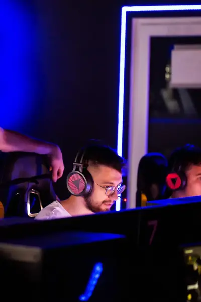 Drie studenten zitten te gamen met gaming headsets op en een docent kijkt mee.