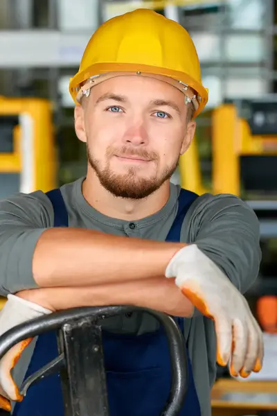 Student met bouwhelm op leunt op machine en lacht in de camera