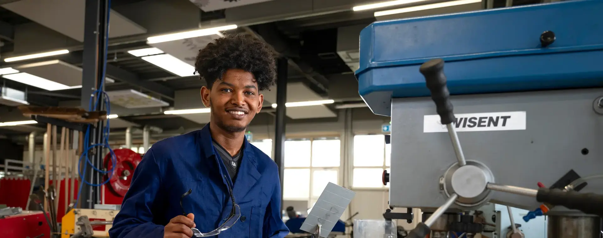 Student in blauw werkpak in een fabrieksomgeving